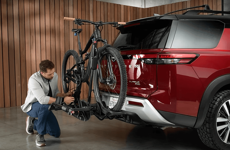 A man crouching by a bike at the rear of a Kia SUV